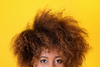 Woman with voluminous curly hair against a yellow background, showcasing the texture and potential for enhancing curl definition with a curly hair protein treatment.